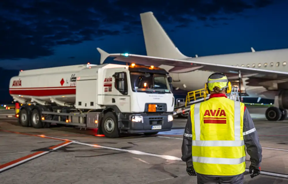 Cysterna drogowa AVIA dostarczająca do samolotu zrównoważone paliwo lotnicze (SAF) na lotnisku, obok pracownik w kamizelce AVIA