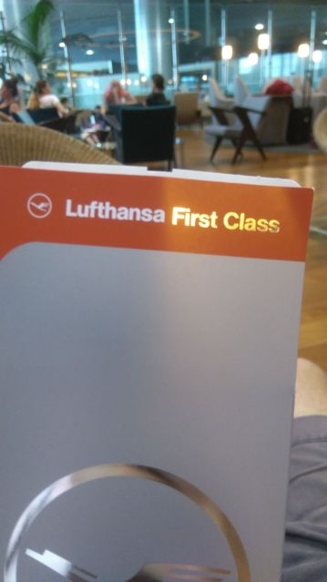 ... machając srebrno  czerwoną kopertą z napisem Lufthansa First Class. - 